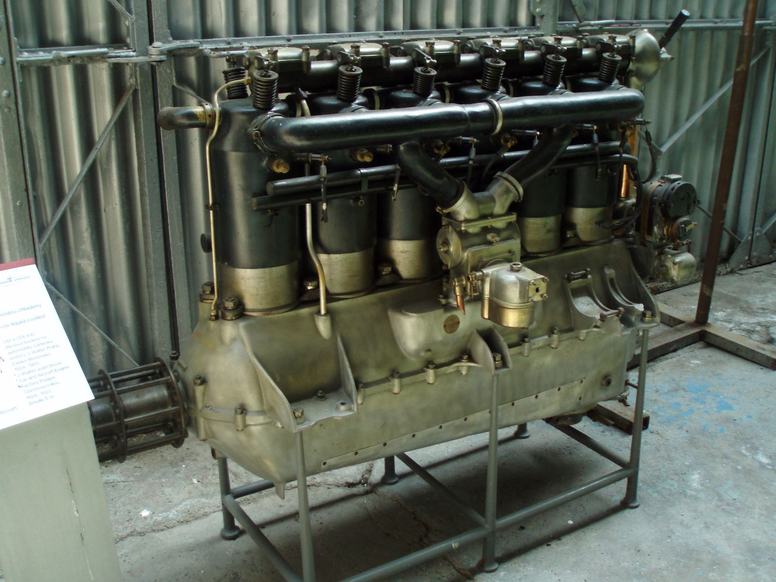 A 1920s six-cylinder in-line aircraft engine on a museum stand, propeller hub at the left.